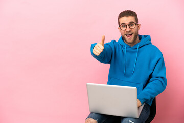 Canvas Print - Young man sitting on a chair with laptop with thumbs up because something good has happened