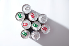 Colorful Drink Cans On White Background, Top View, Hard Light Shadows, Green And Red Pull Tabs