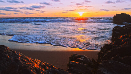 Poster - Beautiful natural landscape with sandy beach  with big stones during sunset.  Sun over horizon and Rolling ocean waves to the rocky shore while sunset.  Summer tourist destination in Portugal. Travel