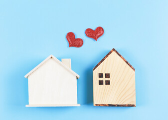 flat lay of two wooden model houses with red glitter hearts on blue background. dream house , home of love, strong relationship, neighboring houses, valentines.