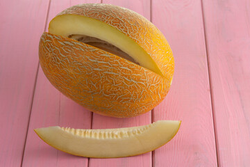 A piece of melon on the background of a cut ripe yellow melon. On a pink background.