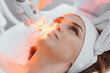 © YURIMA - Red LED treatment. Woman doing facial skin therapy. Radiofrequency face lifting. Hardware antiaging procedure. RF lifting and vacuum massage. A cosmetologist performs a cosmetology procedure