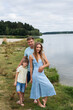 © Ihor - Portrait of a happy family in nature, standing on the banks of a picturesque river. Mom is dressed in a summer dress, dad and son are in shorts and t-shirts.
