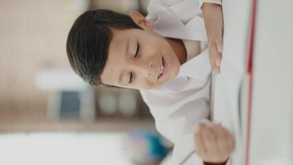 Canvas Print - Adorable hispanic boy student smiling confident writing on notebook at classroom