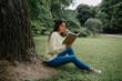 © New Africa - Young woman reading book near tree in park