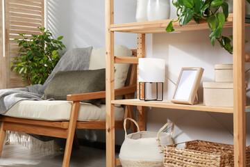 Sticker - Wooden shelving unit with home decor, folding screen and armchair near light wall in room. Interior design