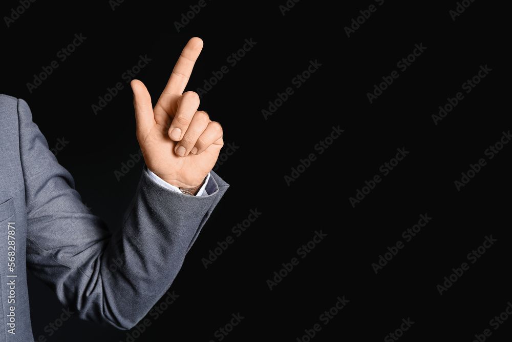Young businessman pointing at something on black background, closeup