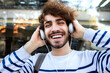 © Daniel - Happy young man relaxing outdoors listening to music using headphones looking at camera.