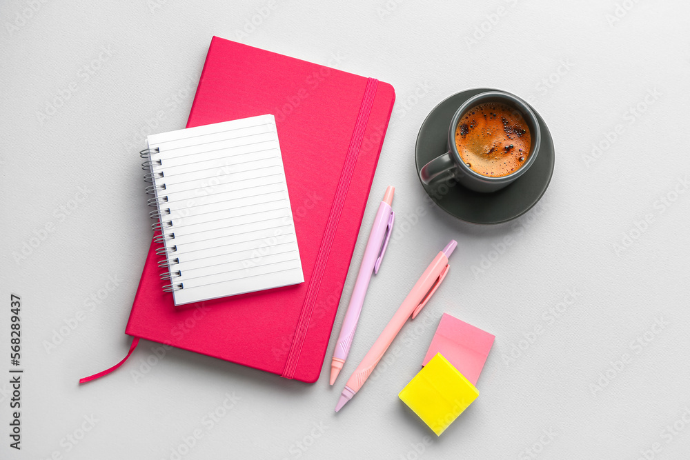 Notebooks, pens, sticky notes and cup of coffee on light background