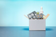 © Sergey - Cardboard box with different medicine pills, tablets and capsules on a blue background with copy space. Buying drug delivery concept.