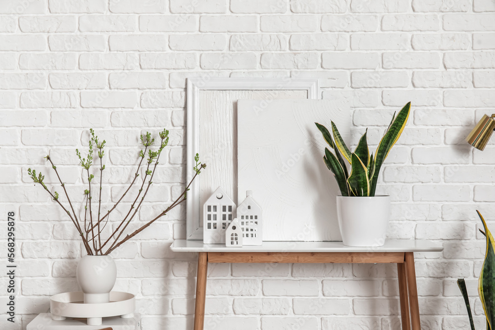 House candle holders on table and houseplants near white brick wall