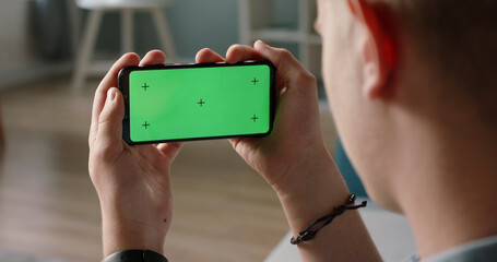 Wall Mural - Man using a smart phone with mock up green screen, talking while having an online conference - online education, communications concept close up 