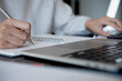 © tippapatt - Close up of woman hand working on laptop computer and writing on notebook with a pen, online working from home. Student studying online class, E-learning, digital education concept
