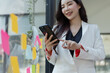 © SOMKID - Asian businesswoman working on smartphone with sticky notes at the office.