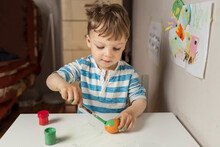 Upper Body Of Blonde Boy Painting Orange Easter Egg With Green P