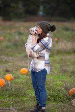 A Young Woman Kissing Her Small Dog In A Pumpkin Patch