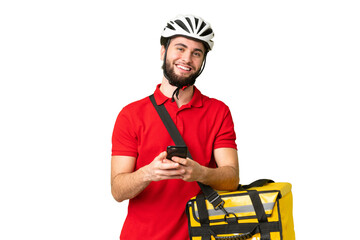 Young delivery man with thermal backpack over isolated chroma key background sending a message with the mobile