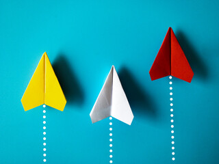 Wall Mural - Yellow, white and red paper airplane origami racing to achieve destination on blue background with customizable space for text. Business goals concept