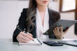 © NINENII - Asian woman hand working at a tablet, computer and writing on a notepad with a pen in the office.