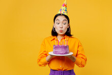 Happy Fun Young Woman In Casual Clothes Hat Celebrate Hold In Hand Purple Cake Blow Out Candles Making Wish In Special Moment Isolated On Plain Yellow Background. Birthday 8 14 Holiday Party Concept