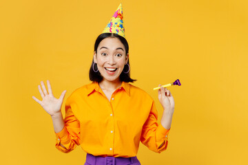 Canvas Print - Happy fun surprised shocked young woman wearing casual clothes celebrating hold in hand blowing pipe look camera spread hands isolated on plain yellow background. Birthday 8 14 holiday party concept.