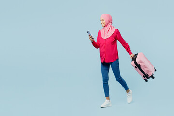 Traveler arabian asian muslim woman in pink abaya hijab hold mobile cell phone bag isolated on plain blue background Tourist travel abroad in free time rest getaway. Air flight trip journey concept.