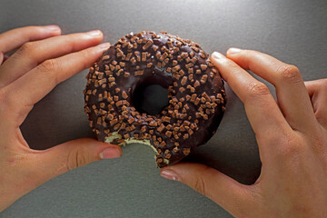 bitten off chocolate donut sprinkled with caramel crumbs in the hands of a teenager on a gray background. View from above. Flatley..