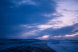 Fototapeta Nowy Jork - Road in iceland with mist on the asphalt surrounded by snow and with snowy mountain in the background at dusk