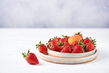 Fresh strawberries and apricot in two ceramic plates on a white wooden table and a gray background. Copy space, close-up.