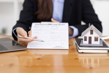 Wooden toy house with real estate agent Asian business woman signs a purchase contract mortgagefor rent sell insurance or loan for a home, Real estate concept.