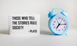 Those who tell stories rule society, Plato quotes the ancient Greek philosopher. Inspirational handwriting on notepad on white background with clock, storytelling concept