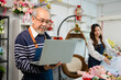 © anon - Elder senior man florist talking on smartphone using laptop at florist.portrait of mature male small business owner using laptop and looking at camera in flower shop