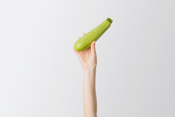 Sticker - Female hand raised up fresh zucchini on a white background