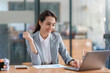 © amnaj - Attractive Asian businesswoman raising hands happily with successful plan with happy smile with laptop computer.