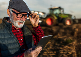 Poster - Senior farmer with tablet in field with tractor in background