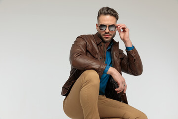 Wall Mural - casual man resting arms, squatting and fixing sunglasses