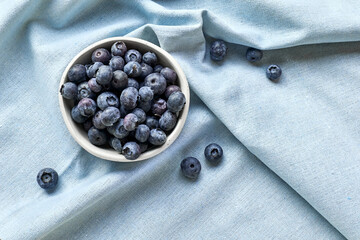 Poster - Fresh organic blueberries. Juicy ripe bilberry in white bowl on blue cloth. Antioxidant and healthy eating concept. Top view.