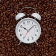 Vintage alarm clock with roasted coffee beans spread out as background.