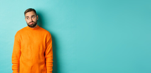 Wall Mural - Sad and gloomy man sulking, looking bored at upper left corner, standing in orange sweater against light blue background