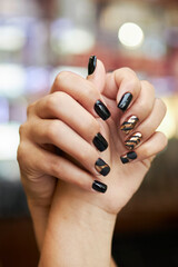 black and gold manicure, hands on a blurred background. Close-up hands of a young woman with a black-gold manicure with rings on her fingers