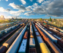 Drone View Of Freight Trains At Sunset. Colorful Railway Cargo Wagons On Railroad. Aerial View Of Colorful Wagons, City, Blue Sky With Clouds. Depot Of Freight Trains. Railway Station. Transportation