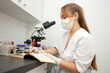 © Богдан Маліцький - girl doctor in uniform and medical mask writes in notebook in the laboratory, a laboratory worker in uniform
