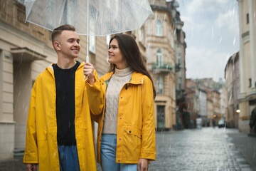 Sticker - Lovely young couple with umbrella walking under rain on city street