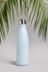 Sticker - Stylish thermo bottle near tropical leaves on light grey background