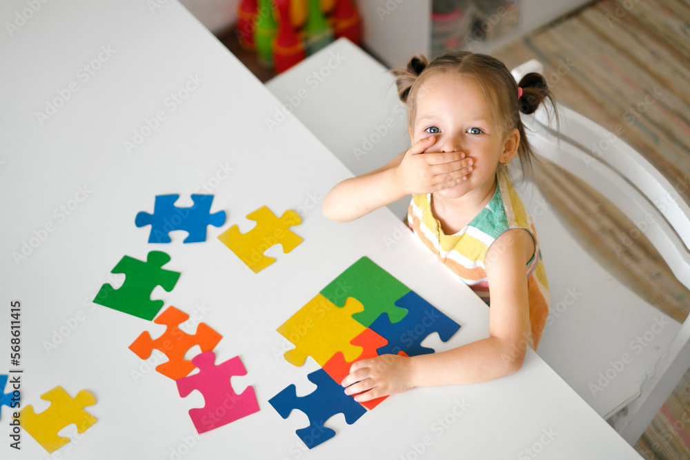A surprised kid is sitting at a table collecting colorful puzzle pieces ...