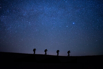Wall Mural - Silhouette small group of young traveler hiking to the top of the mountain with beautiful view star, milky way over the sky. He enjoyed traveling and was successful when he reached the summit.