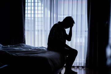 lonely man silhouette sitting on the bed feeling depressed and stressed in the dark bedroom, depress