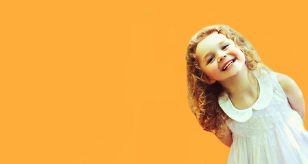 Wall Mural - Portrait of happy laughing little girl child wearing white dress on orange background, blank copy space for advertising text