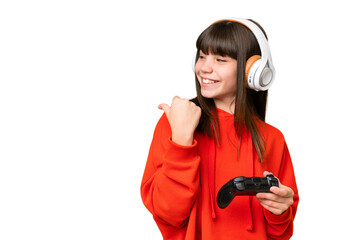 Wall Mural - Little caucasian girl playing with a video game controller over isolated background pointing to the side to present a product