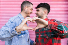 Gay Couple Gesturing Heart Shape In Front Of Pink Roller Shutter